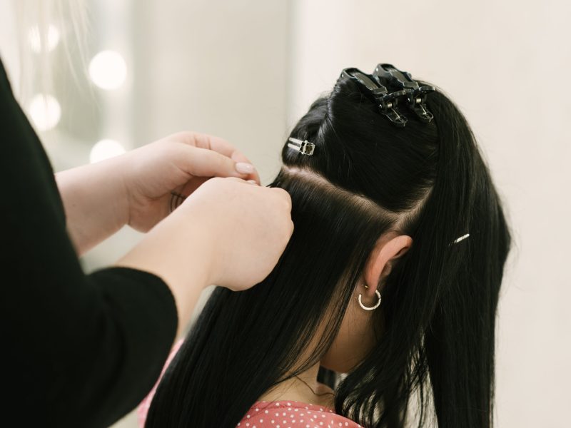 The hairdresser does hair extensions to a young girl in a beauty salon. Professional hair care.